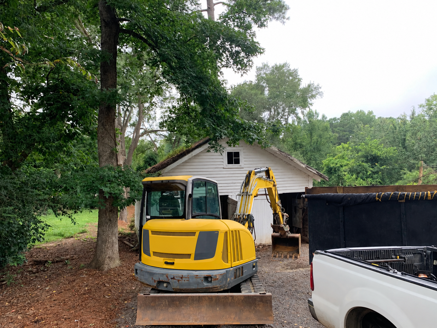 Excavator at garage demolition and cleanup worksite with truck and debris container